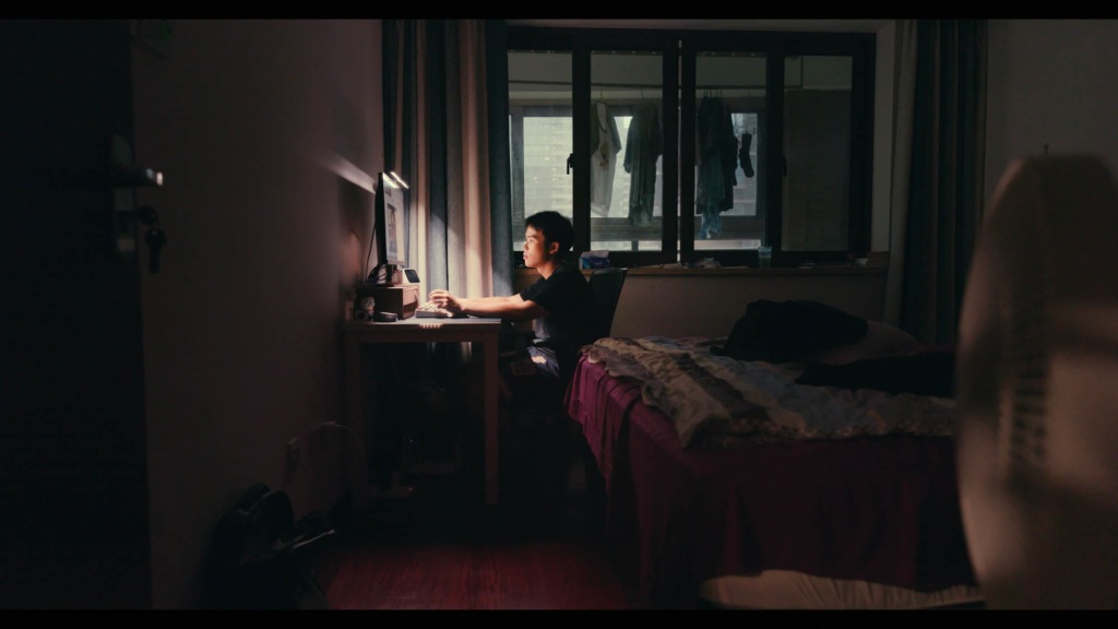 Young man looks at computer screen in dark bedroom