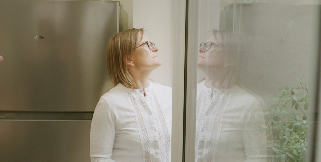 Woman with glasses looks out of house