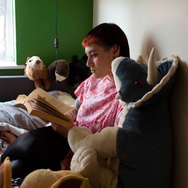 Lady sitting on a sofa, surrounded by soft toys, reading a book