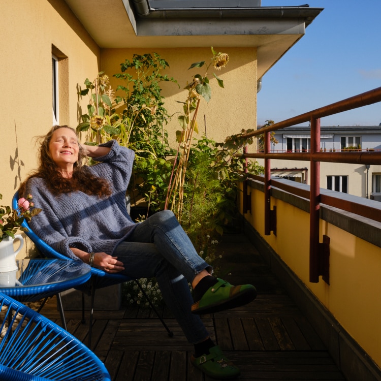 Woman sitting on her balcony, basking in the sunlight, relaxed