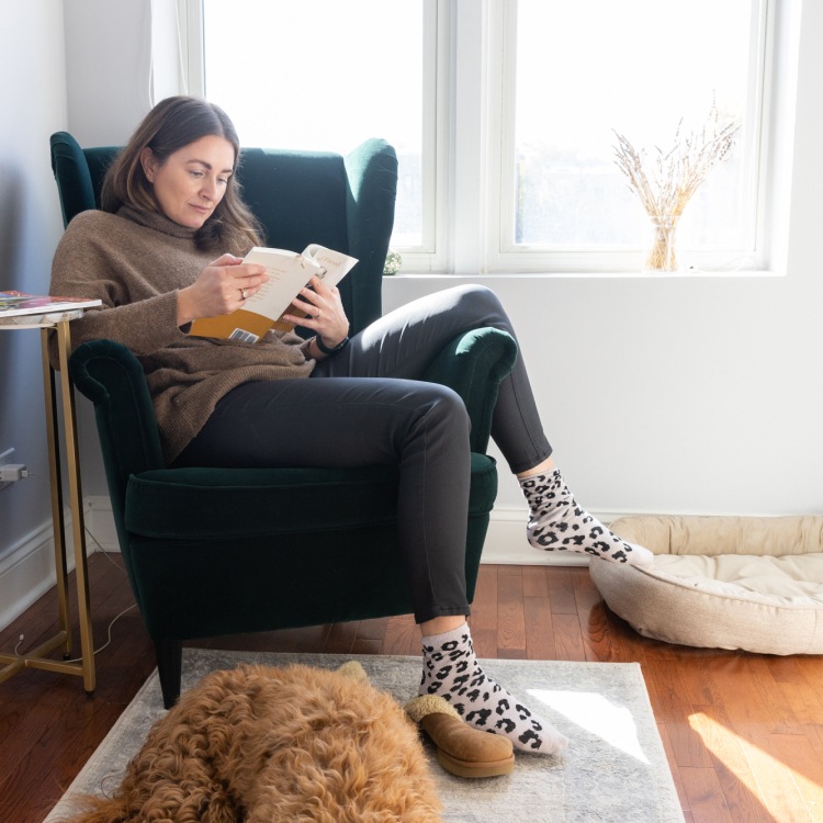 Lady sitting on quiet armchair, reading a book with her dog sitting at her feet