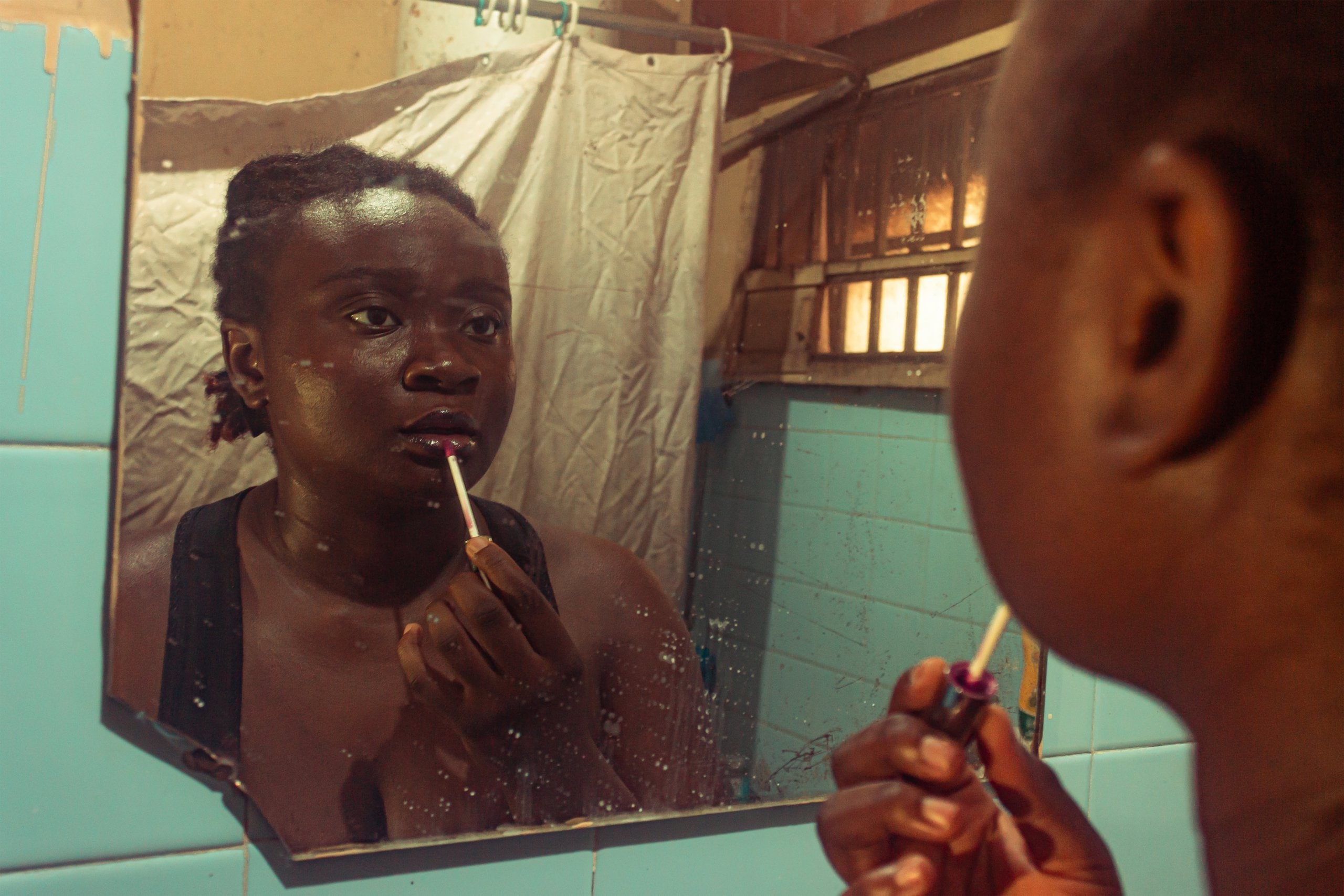 Ife putting on lip-gloss looking in the bathroom mirror.
