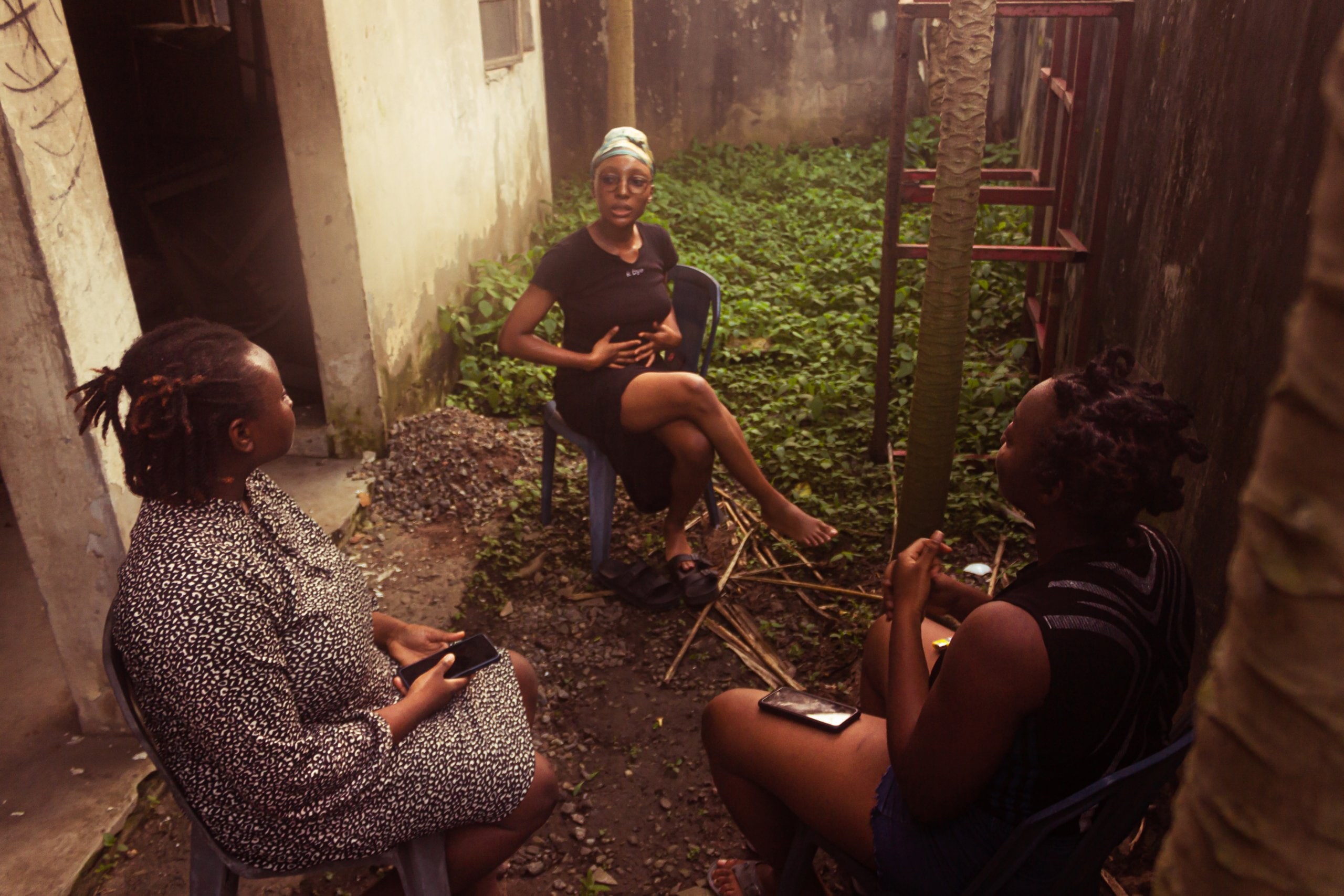 Ife and two women sits outside in the backyard.
