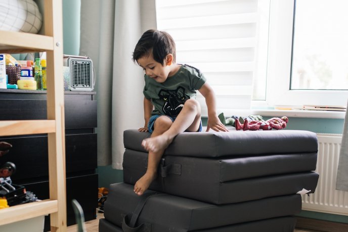 Young boy jumping around his bedroom furniture