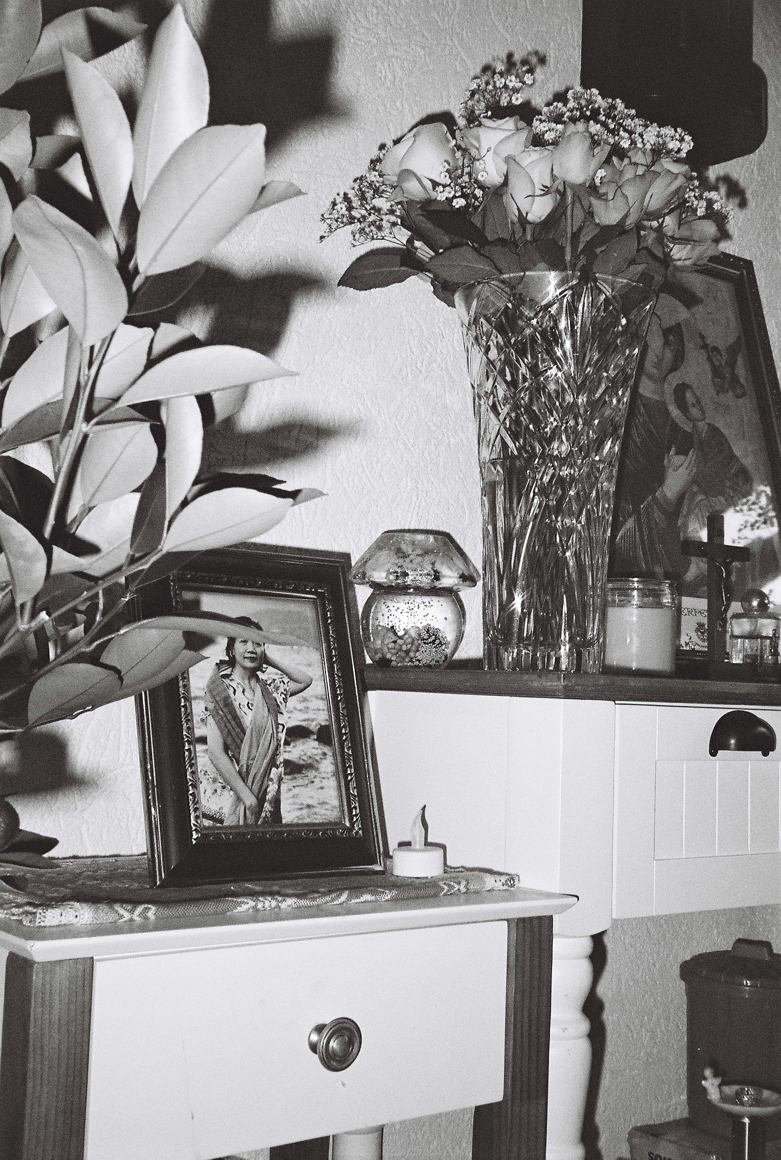 A glass vase with roses, next to it a framed photo of a woman.