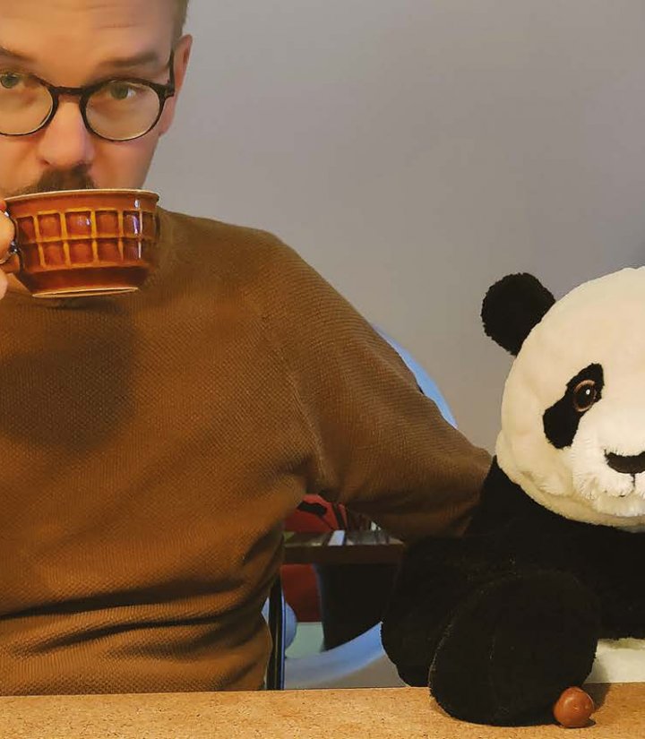 Man drinking tea, sat with cuddly toy panda