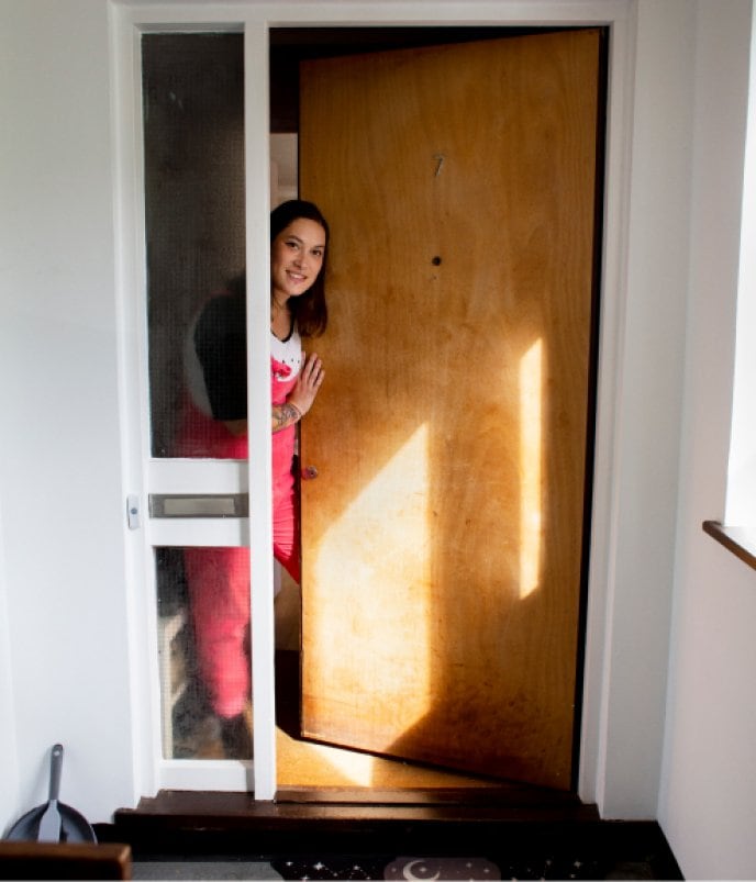 Lady opening the door to her home, looking happy.