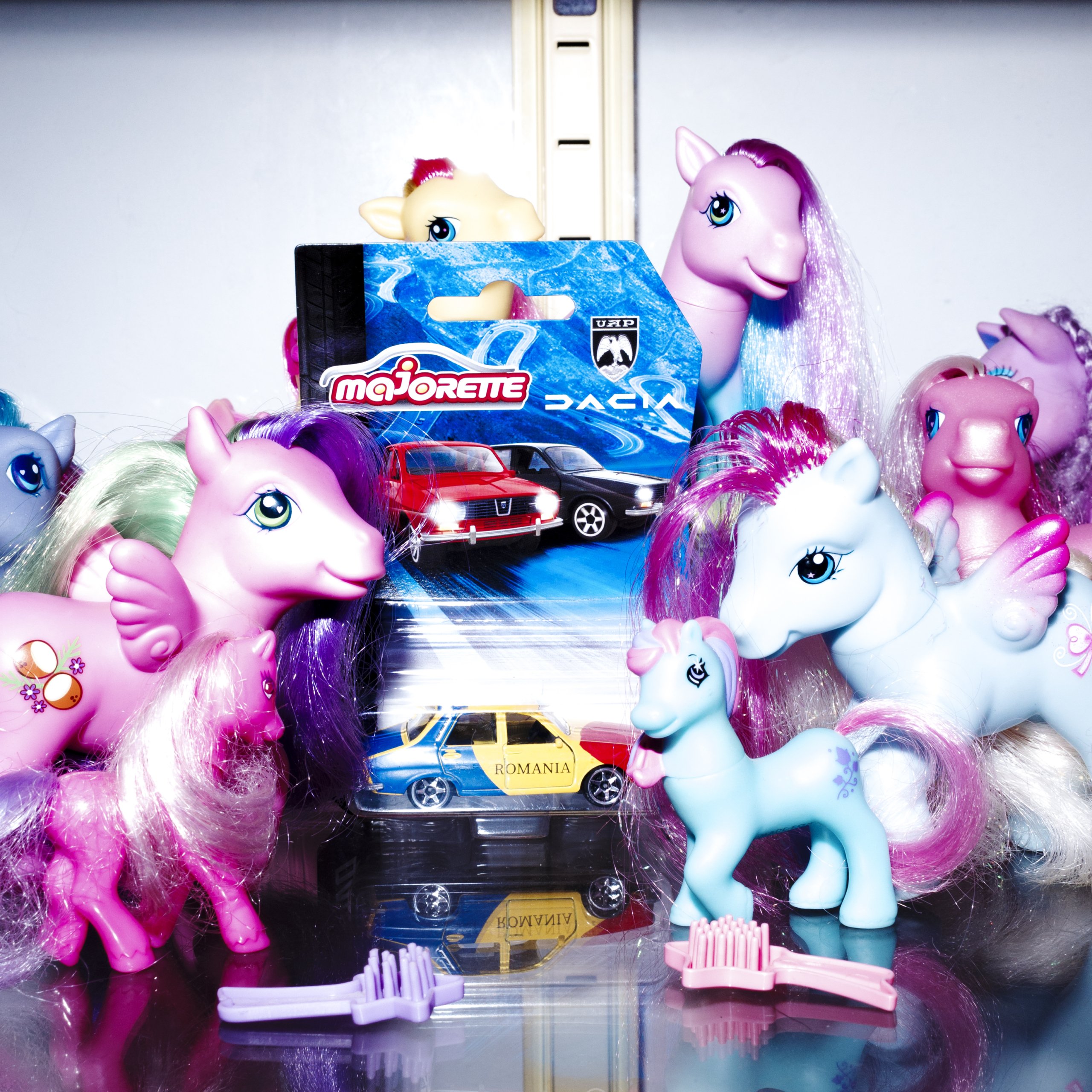 My little ponies surrounding a toy car still in its package.