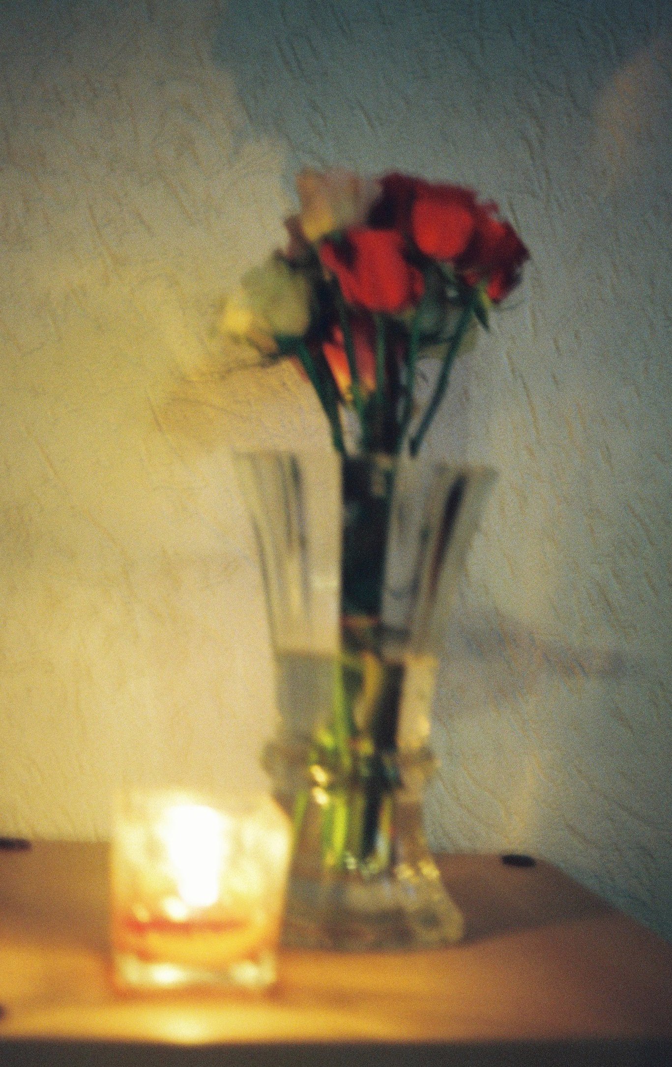 A blurry photo of roses in a vase and a candle light.