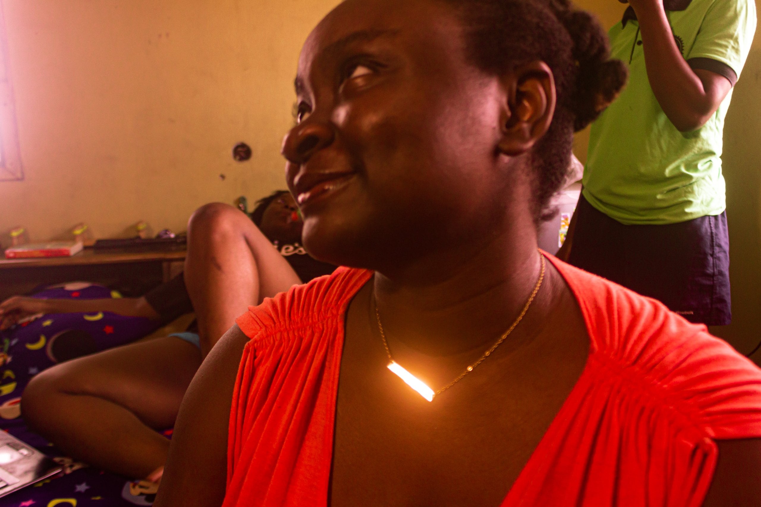 Ife wearing a gold necklace and a red dress, family members standing behind her.