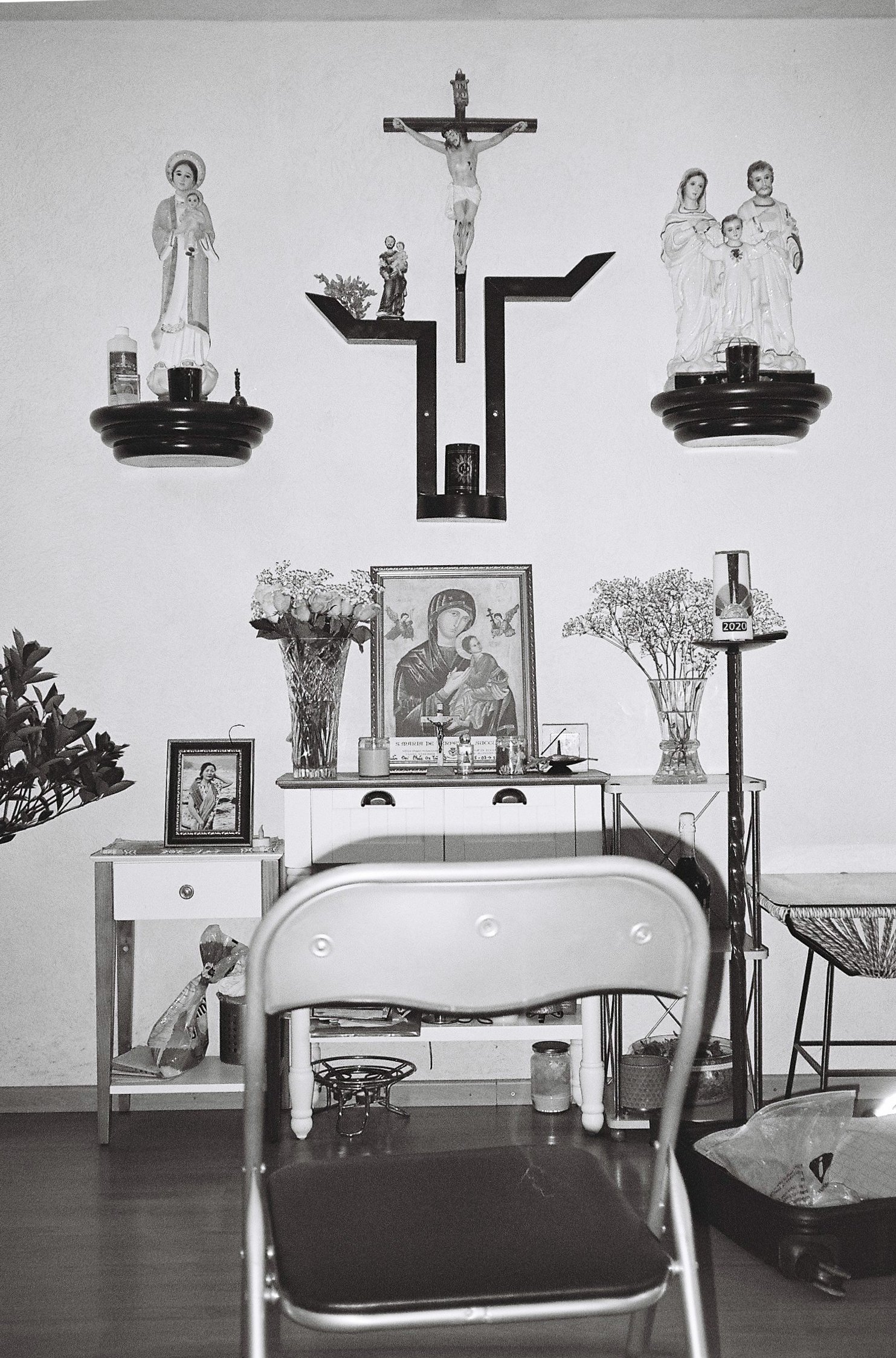 Christian symbols, statues and pictures on a wall with a chair standing in front of it.