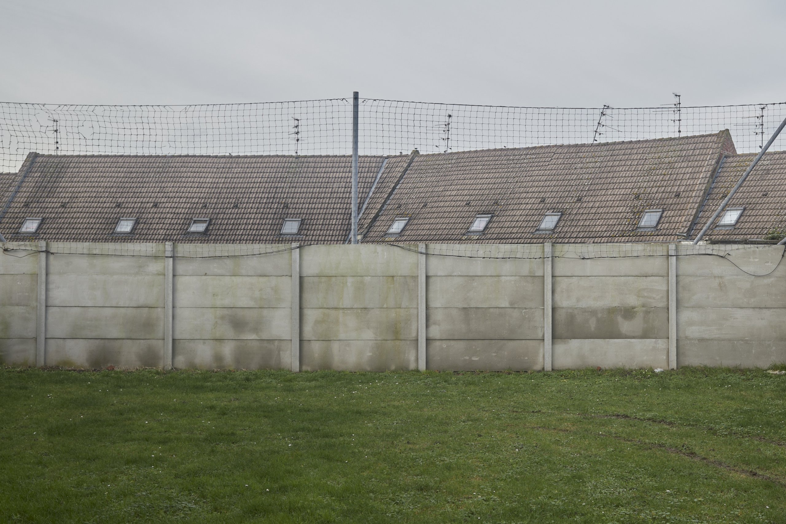 A grey concrete wall with a net fence on top.