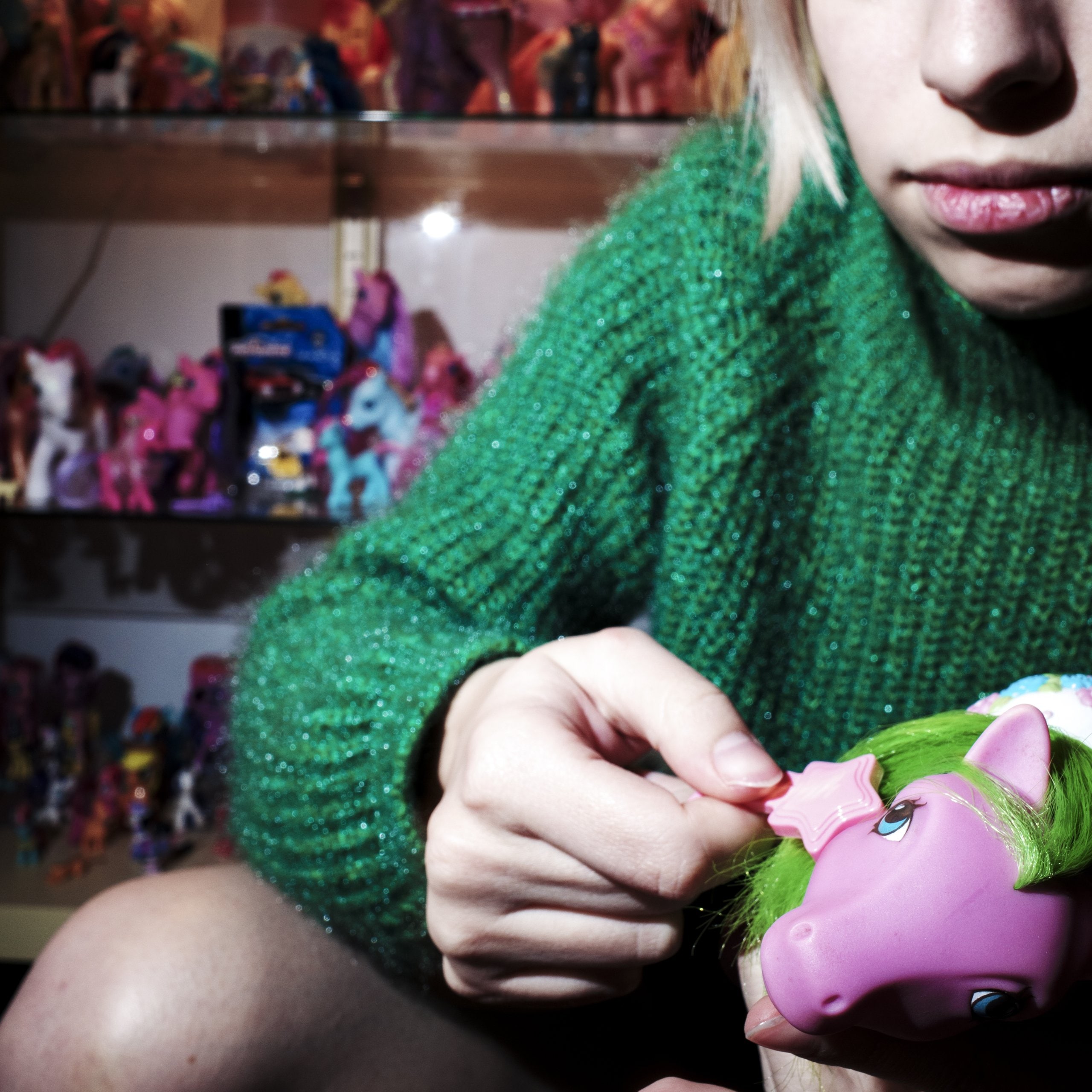Toma's girlfriend brushing the green hair of a pink My little pony, behind her is shelves full of more My little ponies.